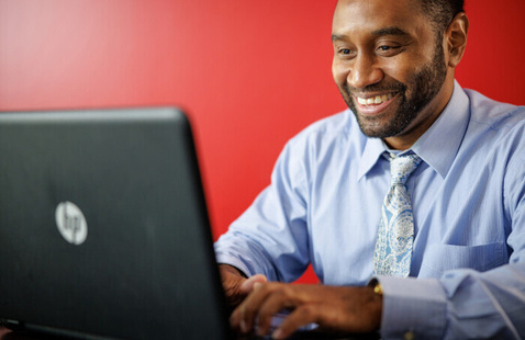 A man wearing a button-down shirt and tie works on a laptop