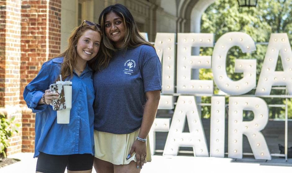 Two Students standing in front of large Mega Fair light up letters