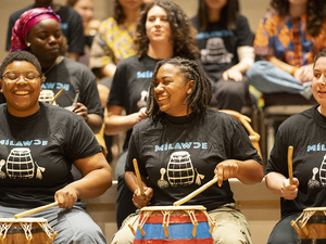 Students smiling while performing with the Five College West African Music Ensemble.
