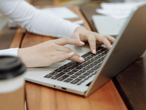 Close up of someone typing on a laptop, a coffee nearby.