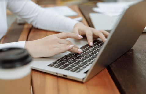 Close up of someone typing on a laptop, a coffee nearby.