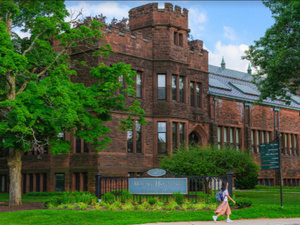 A student walks in front of Dwight Hall by the Mount Holyoke iron gate.