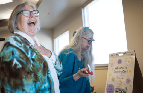 Two women smiling in front of Stepping On program materials.