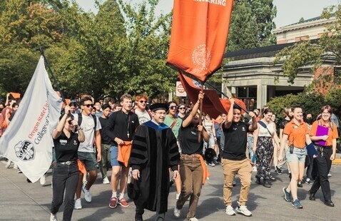 A group of new students walking in procession behind a College of Engineering banner.