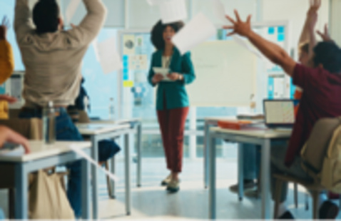 A stock image of a classroom, with students at their desks throwing papers in the air in celebration.