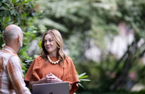 Man and woman talking, with the woman holding a laptop on her lap