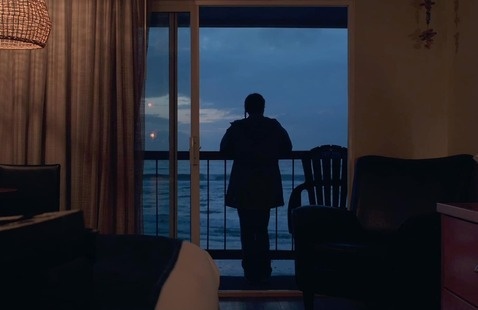 Still from małni – towards the ocean, towards the shore: a silhouetted figure stands on a balcony overlooking the ocean at dusk
