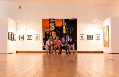 Photo of a family enjoying Art from Abstract to Zion Exhibition at SUMA. The family is sitting on a bench in front of a large tapestry.