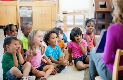Children laugh while teacher reads book