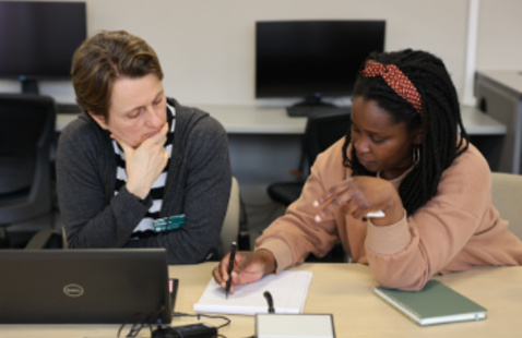 A student and a library expert sit together in the cmd lab over a laptop and a note pad.