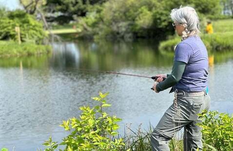 Woman on the waters edge holding a fishing rod