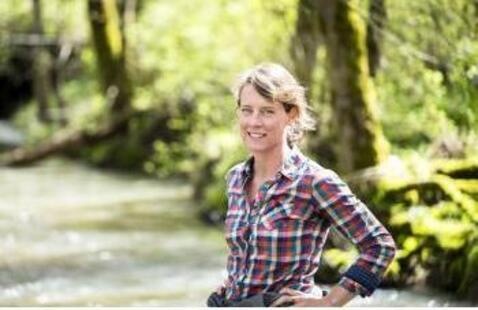 A woman in a plaid shirt standing in the forest by a river
