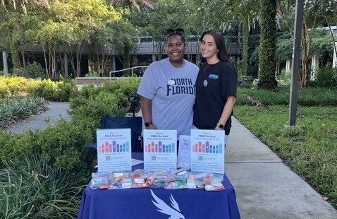 Two students standing at outside event table