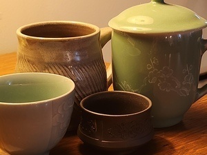 Ceramic tea pot and mugs arranged together on wooden table.