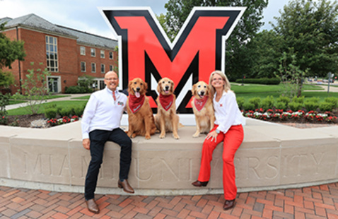 Greg and Renate Crawford and dogs Ivy, Newton, and Charlie pose at the RedHawk Plaza large beveled M