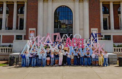 Large group of sorority girls holding up wooden Greek letters representing their houses. 