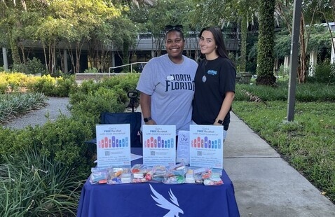 Two students standing at outside event table