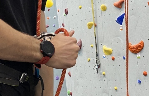 A person standing near a climbing wall holding a rope.