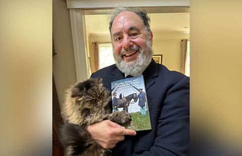 Appears to be a heashot of Brad Stone with a pet and a book.