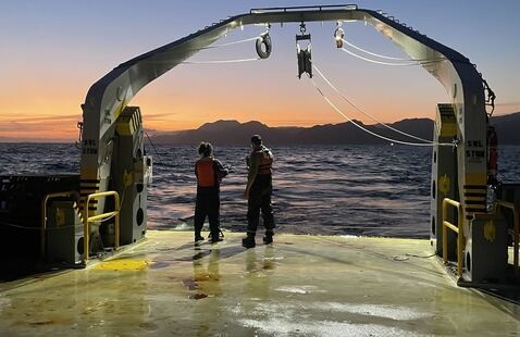 Two oceanographers on a ship sampling at sunset