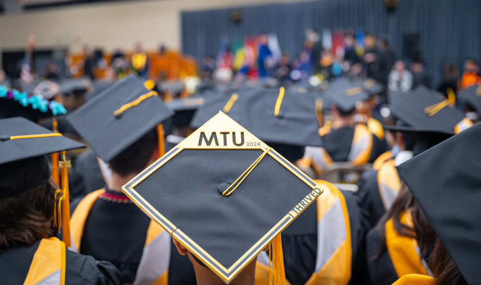 Cap with MTU design on it amid the graduates at commencement.