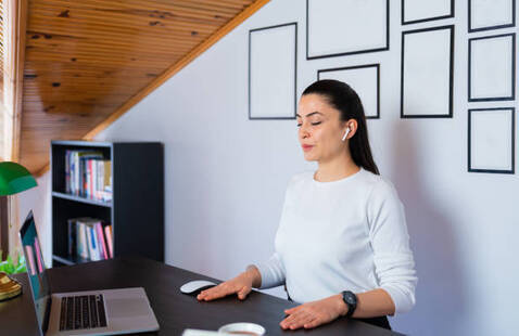 Woman sitting at a desk with eyes closed and hands on her desk. 