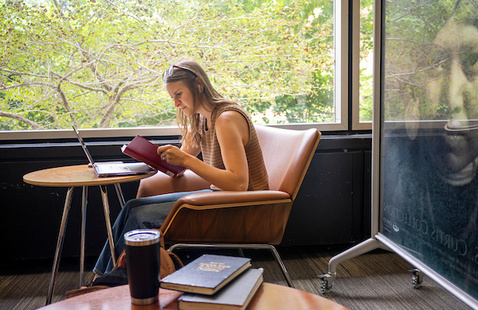 Students sitting at table in front of laptop, holding book