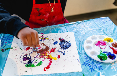 Child wearing a red smock painting a picture