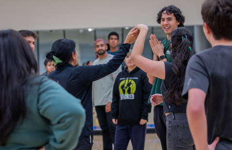 Group practicing salsa in a mirrored studio; instructor guides partner's arm for a turn while others watch