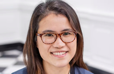 Person wearing tortoiseshell glasses smiling at camera in an indoor room with white walls and black-and-white checkered floor