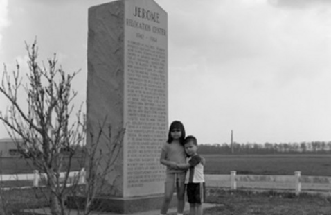 Two children standing together beside a tall stone monument that memorializes the Jerome Japanese Internment Camp.
