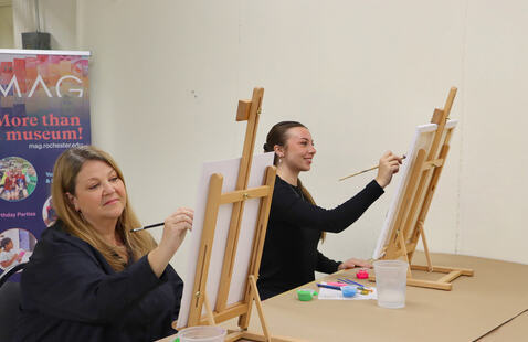 Two adult students painting at easels in the Creative Workshop.