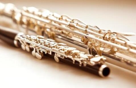 Close-up of two silver concert flutes lying on a light surface, keys and open headjoint visible