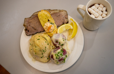 Top-down plate of potatoes and prime rib with a cup of hot cocoa and mini marshmallows.