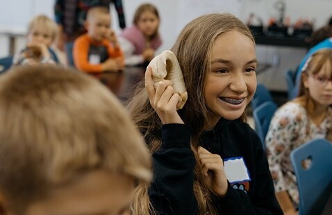 A young person holds a bone to their ear.