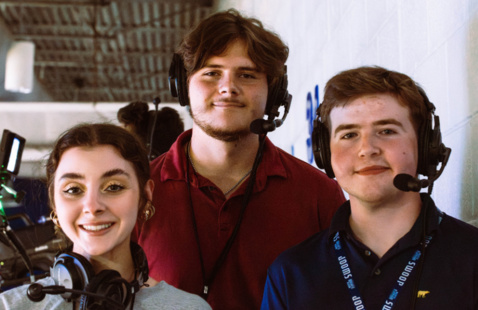 Three Spinnaker students are looking at the camera, with broadcast headsets on, before a UNF basketball game