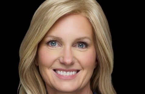 Professional headshot of a person with blond hair in blue blouse against a black background. 