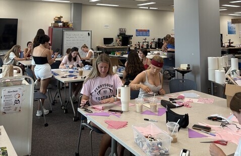 Students at tables cutting paper and assembling decorations in a classroom makerspace, craft supplies and drinks
