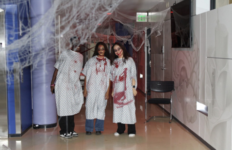 Three students in hospital gowns and fake blood and cobwebs in Skinner Hall.