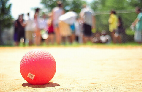 A kickball sits in the foregound as players talk in the background.