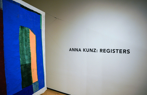 Gallery wall text 'ANNA KUNZ: REGISTERS' beside a large abstract painting with blue, green and orange shapes.