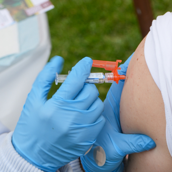 Blue-gloved healthcare worker administering a vaccine into a person's upper arm with a syringe