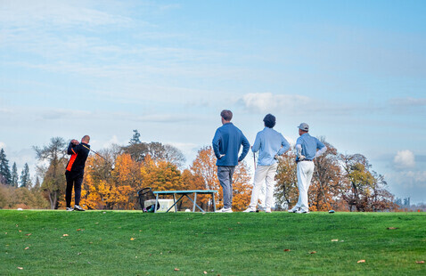 A parent swings a driver while a family watches at Trysting Tree Golf Course