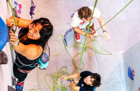 A student climbs up the Dixon Climbing Center rock wall while a student belays them from below.
