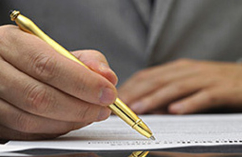 a hand holds a gold pen and writes on a piece of paper
