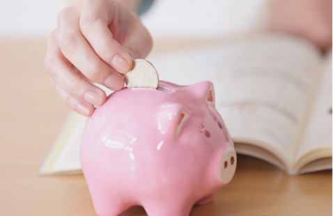 A hand putting a coin into a pink piggy bank