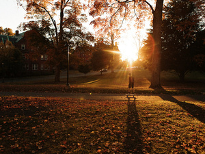 A student skate boards across campus at sunset.