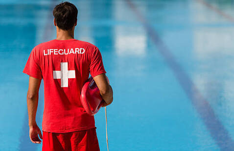 A lifeguard stands in front of a pool.