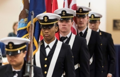 5 military members standing in like next to flags