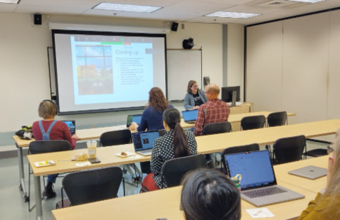 People sitting in a room watching a speaker with a presentation open on a screen